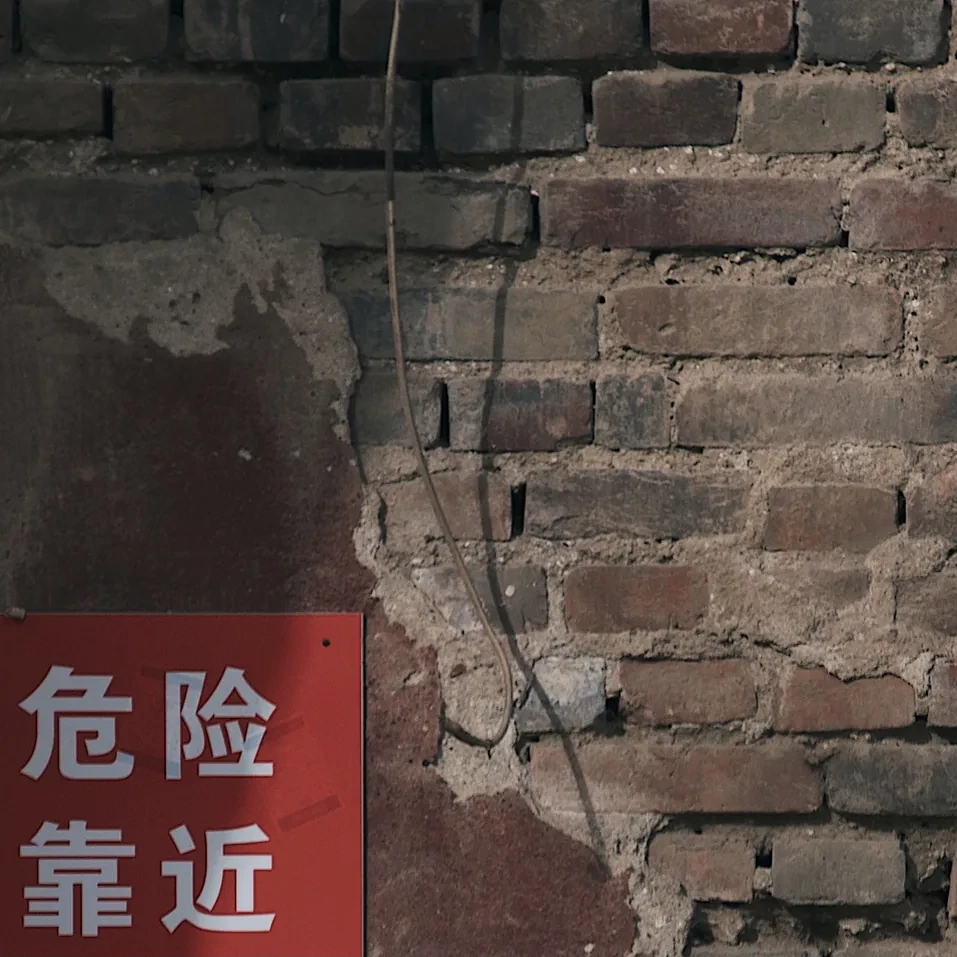 A red danger sign on an old Beijing brick wall.