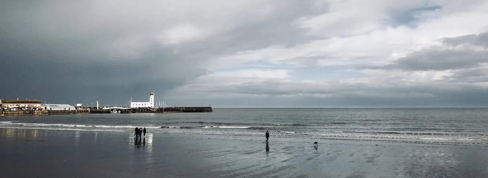 Small figures walking on a reflective Brighton beach.