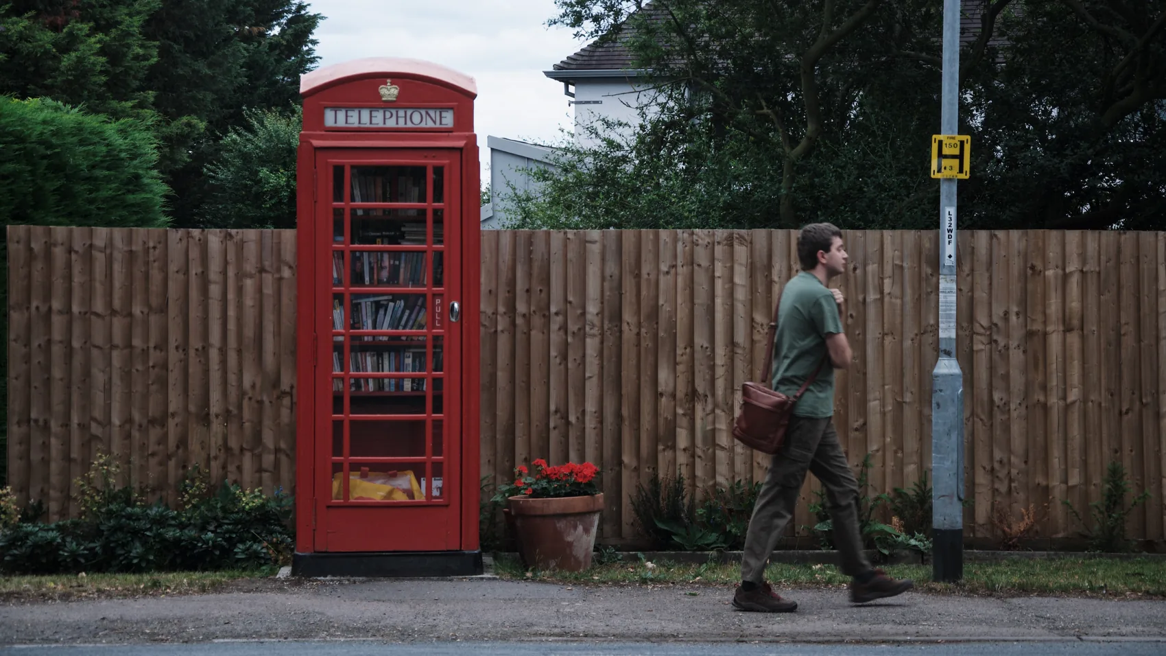 A pedestrian passing a red phone box on a quiet Cambridge road.