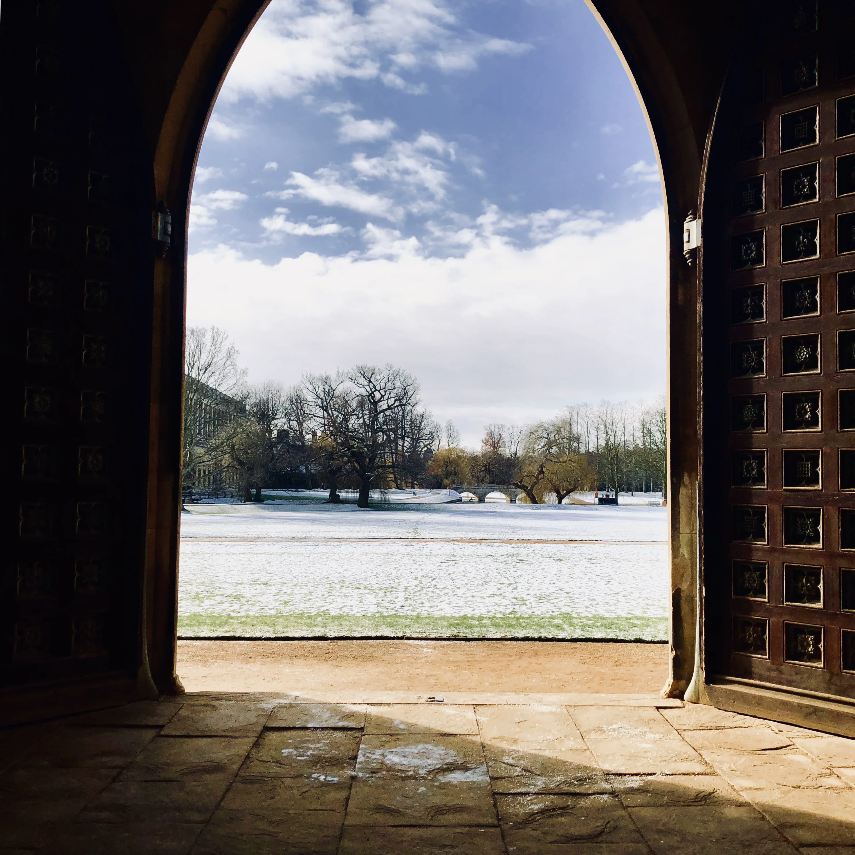 A snowy Cambridge court seen through a stone archway.