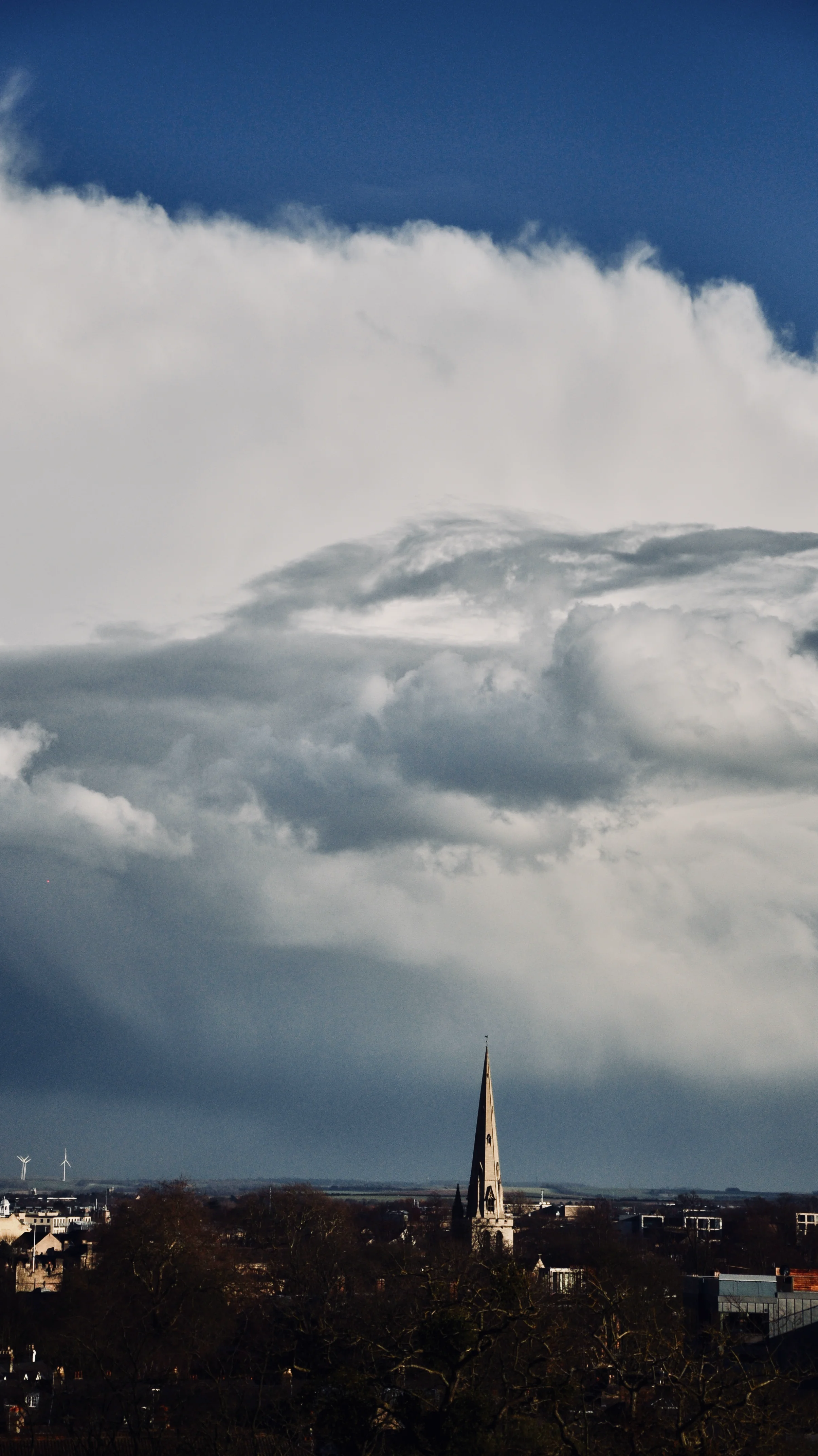 A Cambridge spire beneath a towering wall of cloud.