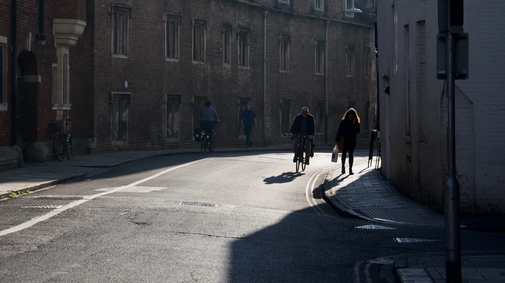 Two figures walking through a curved Cambridge street shadow.