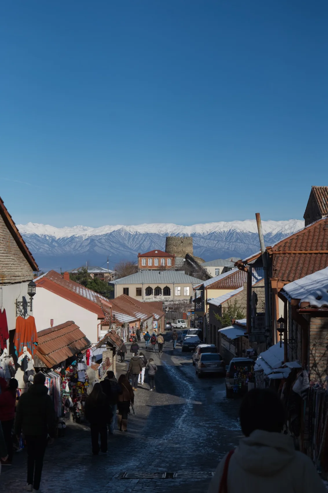 A Georgian village street with snowy mountains beyond.