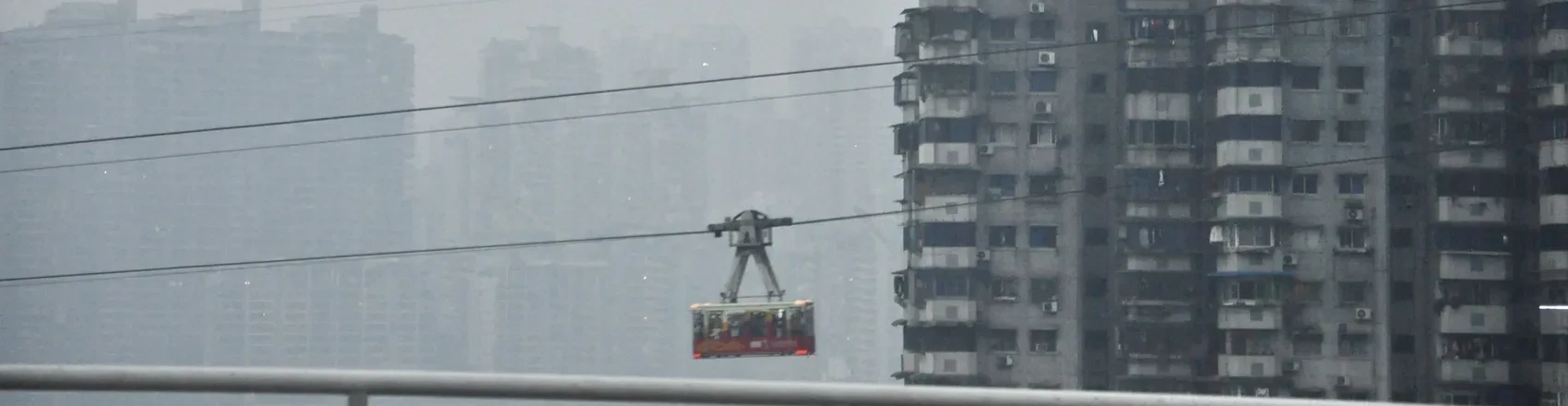 A Chongqing cable car cutting through fog between buildings.
