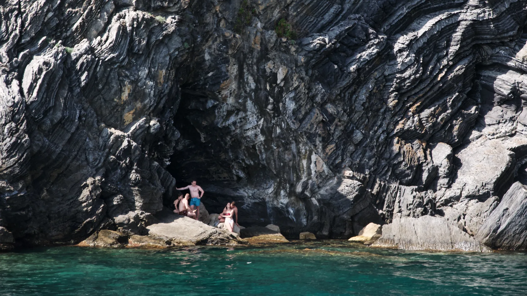 Swimmers beside dark Cinque Terre rock and green water.