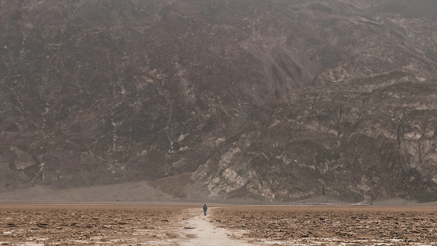 A tiny walker on the Death Valley salt flats beneath dark mountains.