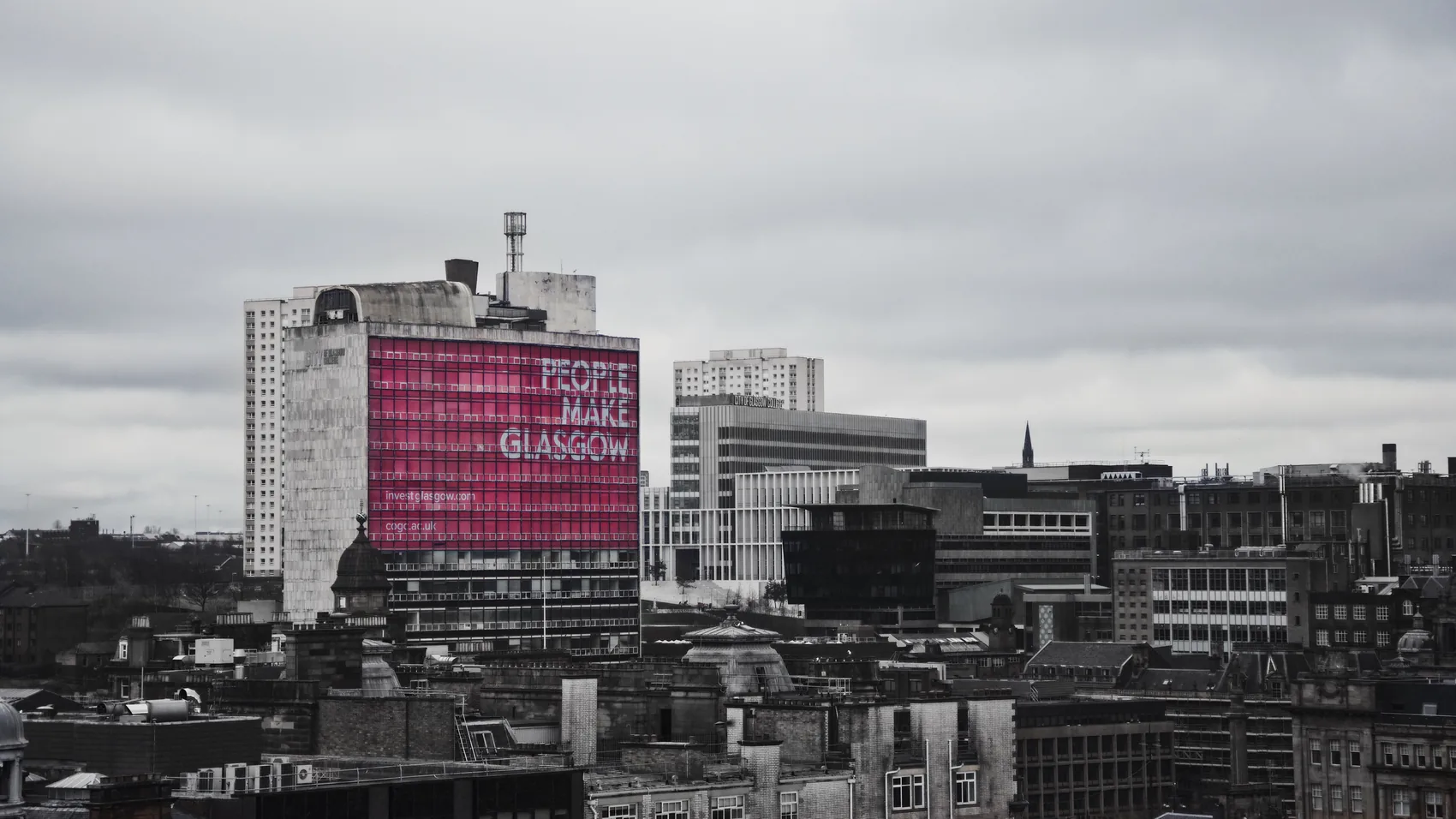 A pink billboard punctuating a black-and-white Glasgow skyline.