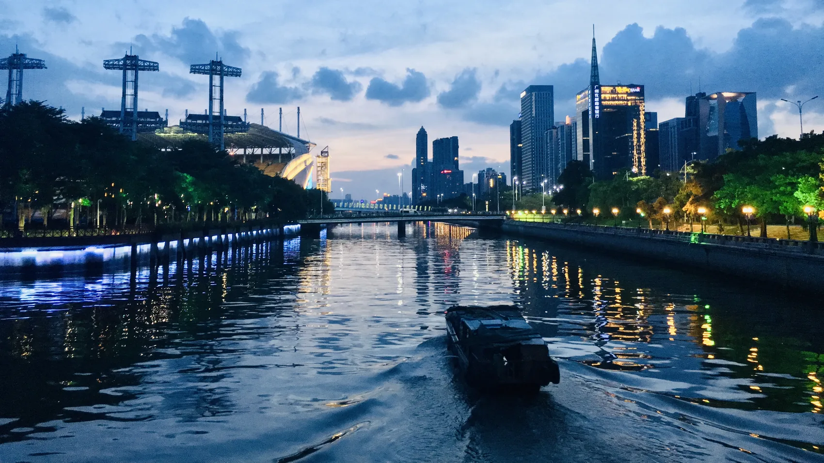 A boat crossing the Guangzhou river under a blue city evening.