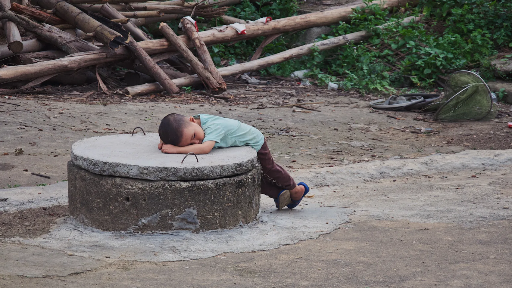 A child resting on a circular well in a Huazhou courtyard.