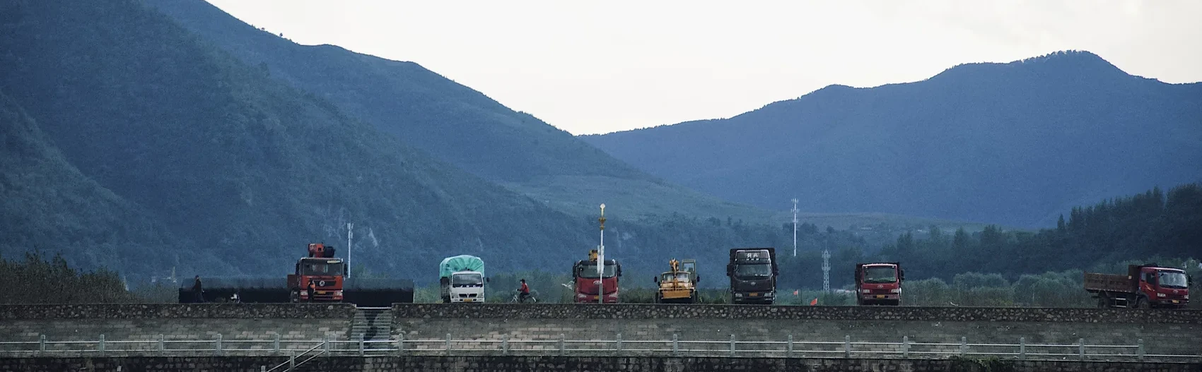Cars lined along a dam beneath blue Jilin mountains.