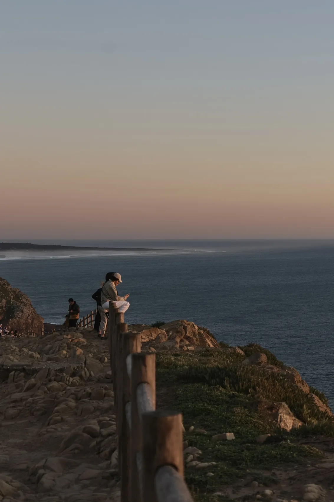 A person standing on a headland near Lisbon at sunset.