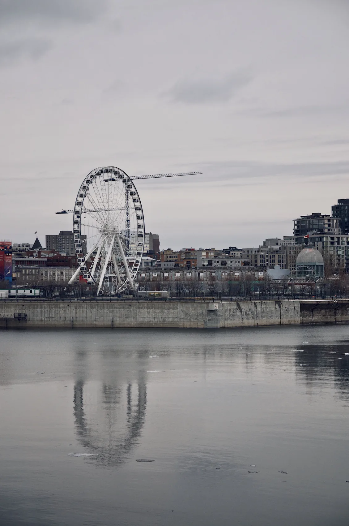 A Montreal waterfront ferris wheel reflected in still water.