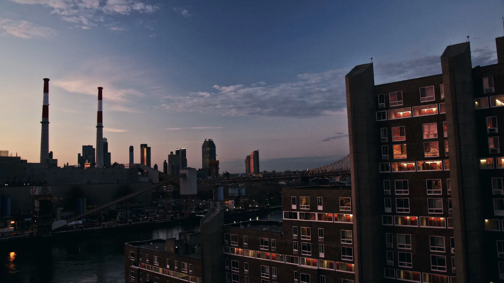 Industrial stacks and New York buildings at dusk.