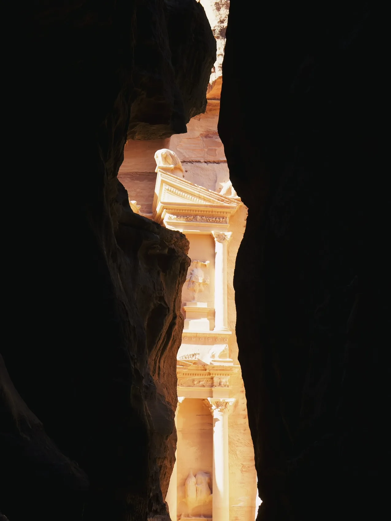 The Petra Treasury glimpsed through a dark canyon slit.