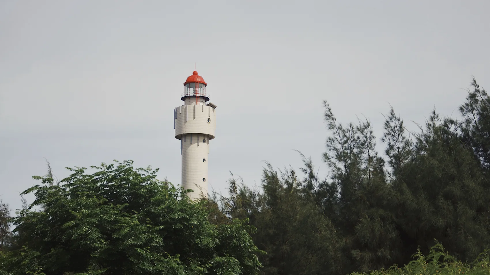 A Shanwei lighthouse rising behind green trees.