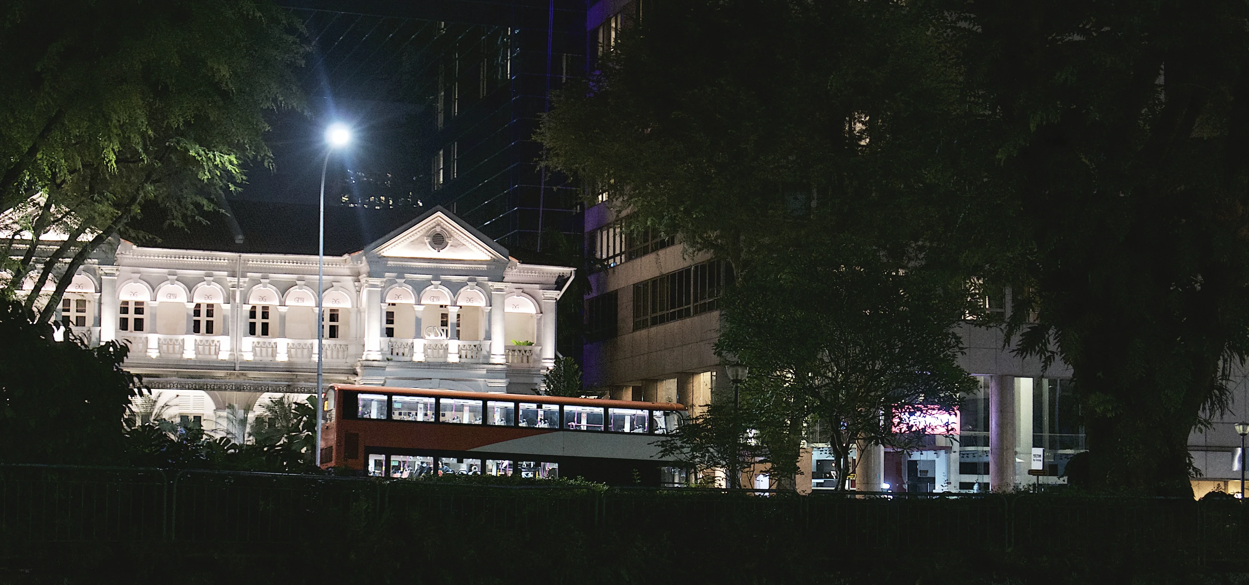 A lit colonial building and double-decker bus at night in Singapore.