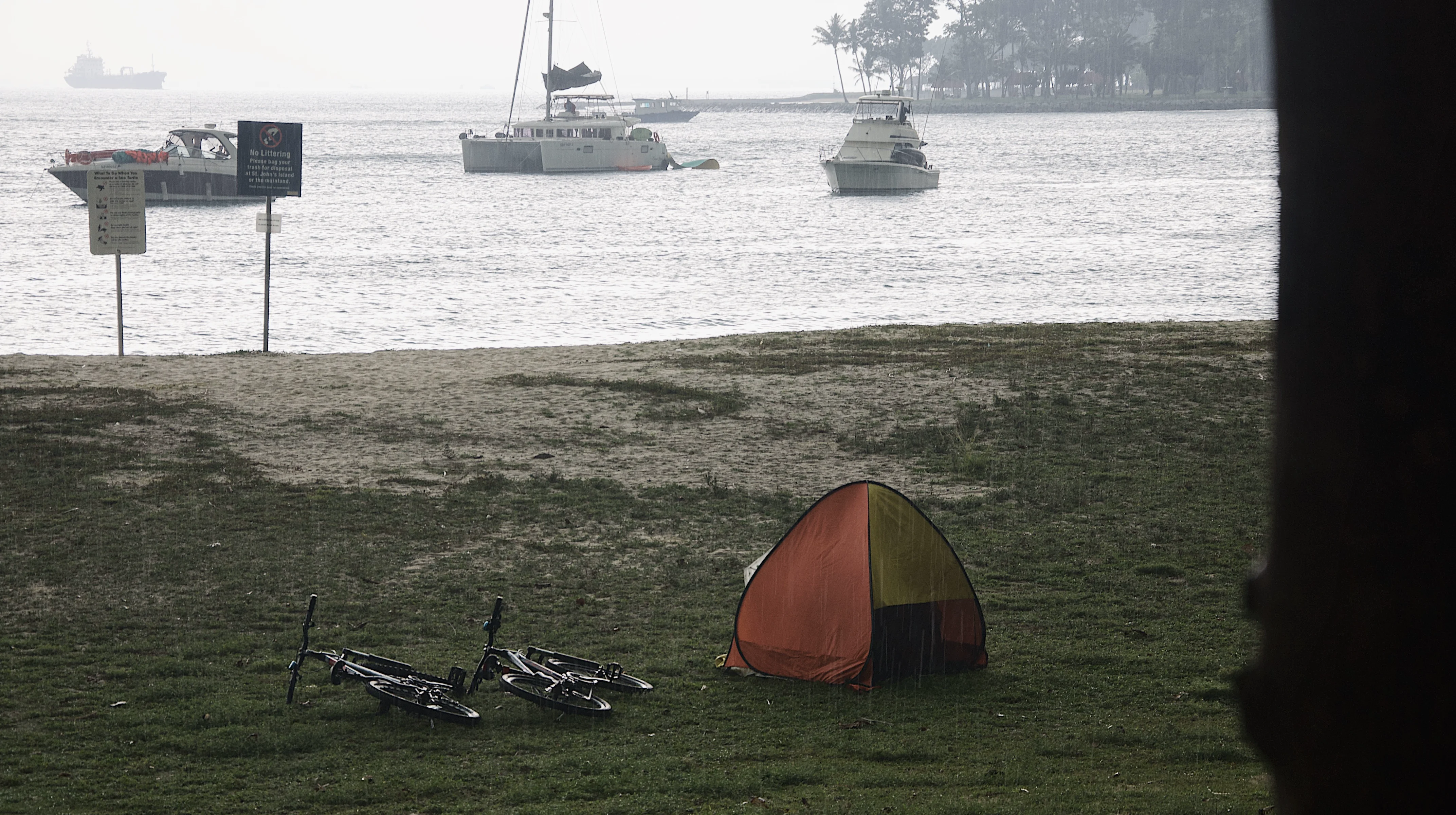 A tent and bicycles on a Singapore island shore in rain.