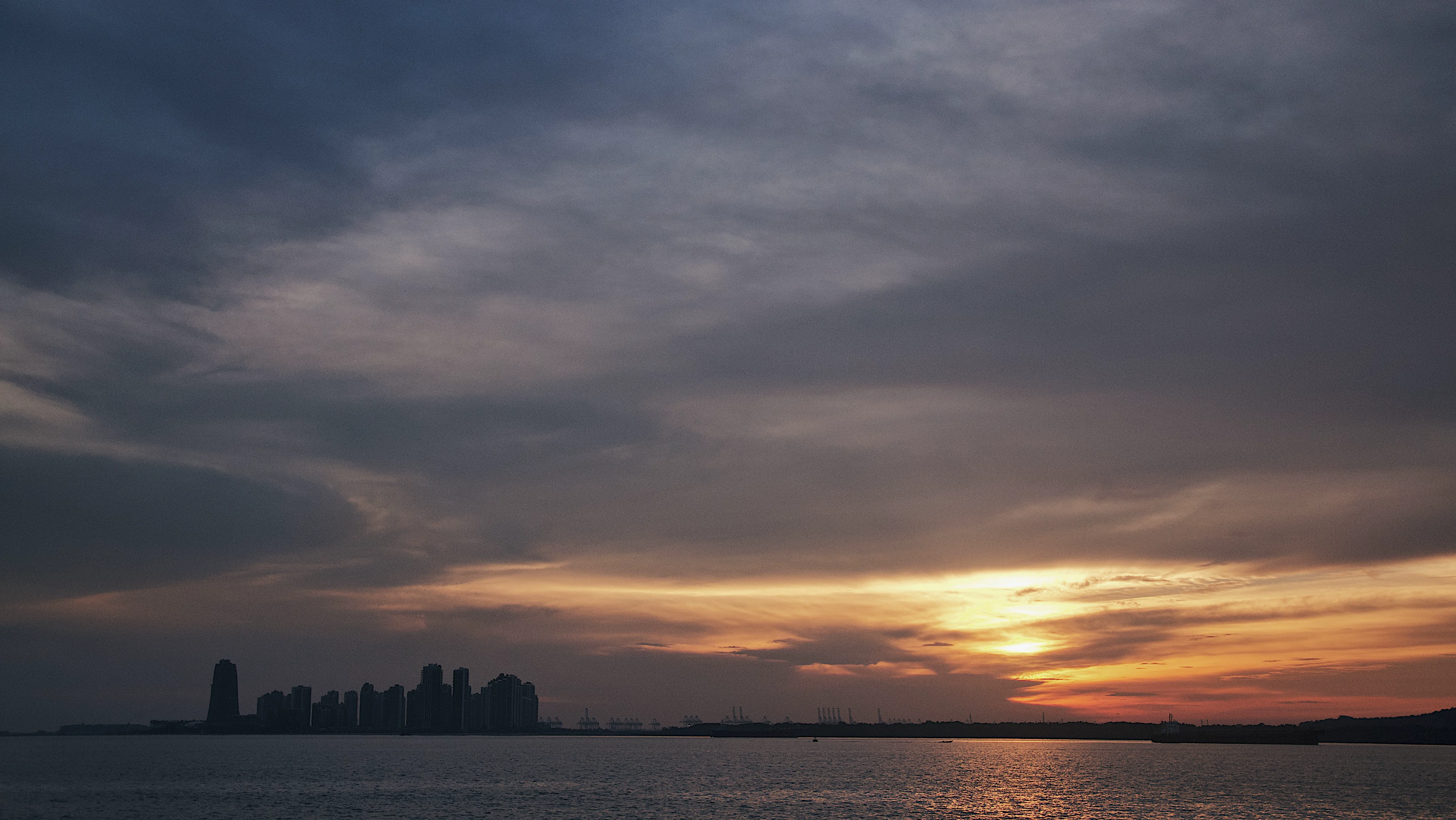 Singapore skyline in silhouette at sunset over the strait.