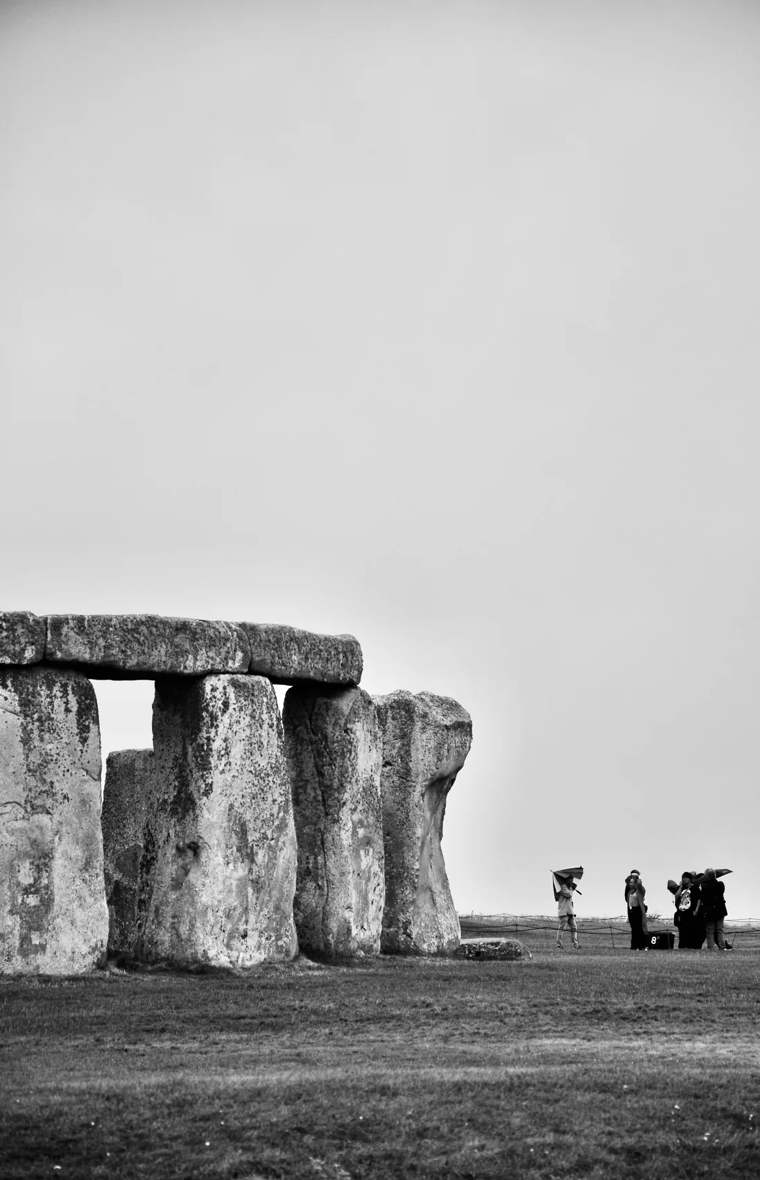 A black-and-white view of Stonehenge with small visitors at the edge.