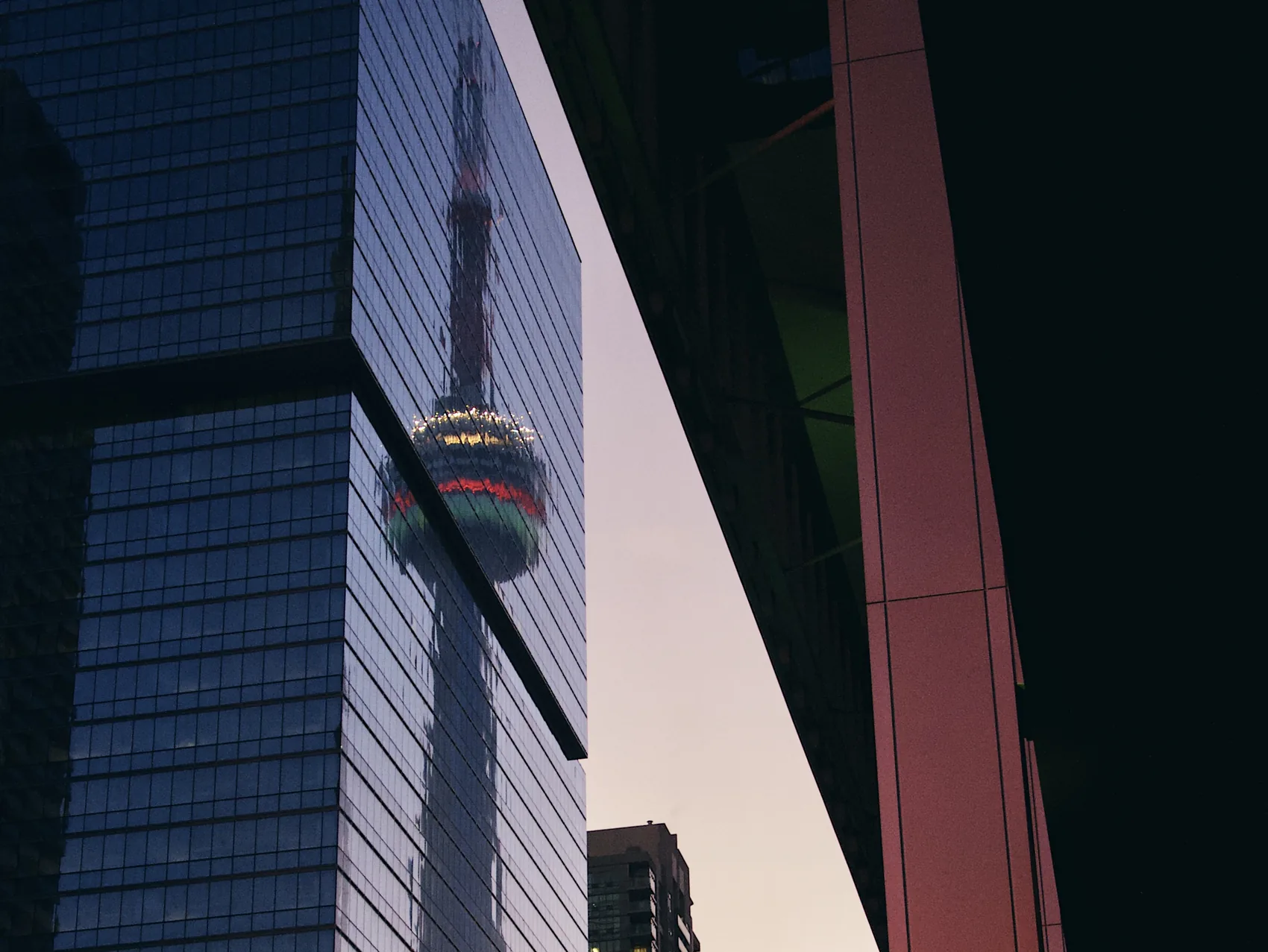 The CN Tower reflected in a dark Toronto glass facade.