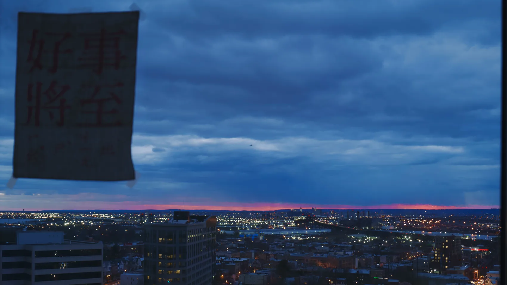 A note taped to a window over a stormy city view.