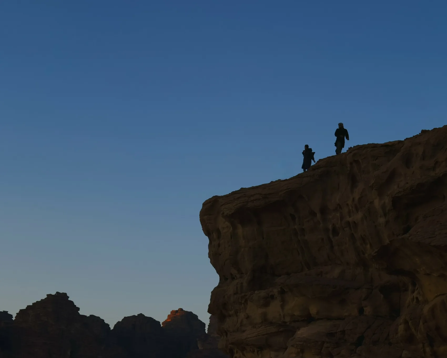 Small figures standing on a Wadi Rum ridge against blue sky.