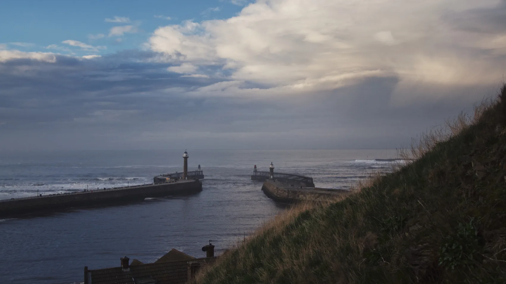 Whitby harbour mouth at dusk with the sea opening beyond.