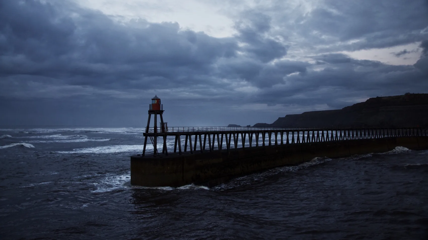 Whitby lighthouse and pier under blue-grey cloud.