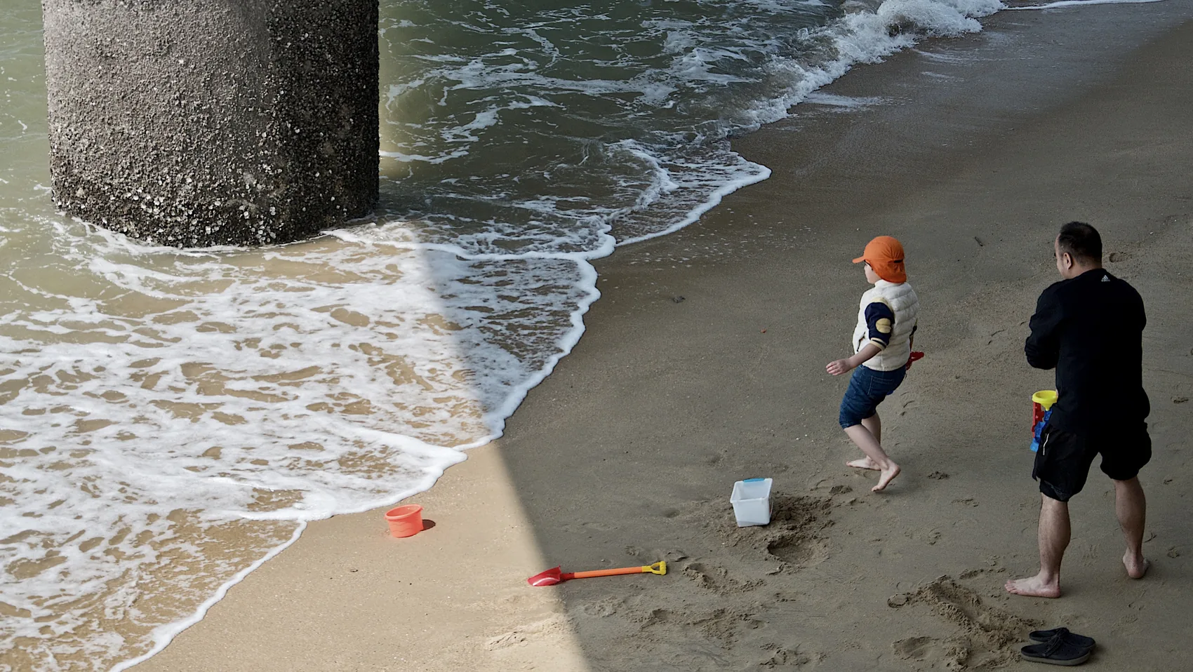 A child and adult at the Xiamen shore under a concrete column.